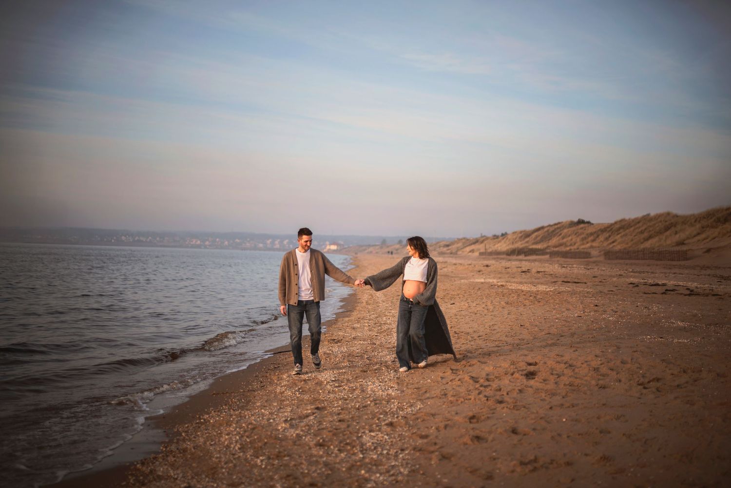 Romantic couple holding hands while walking on a beach during golden hour.