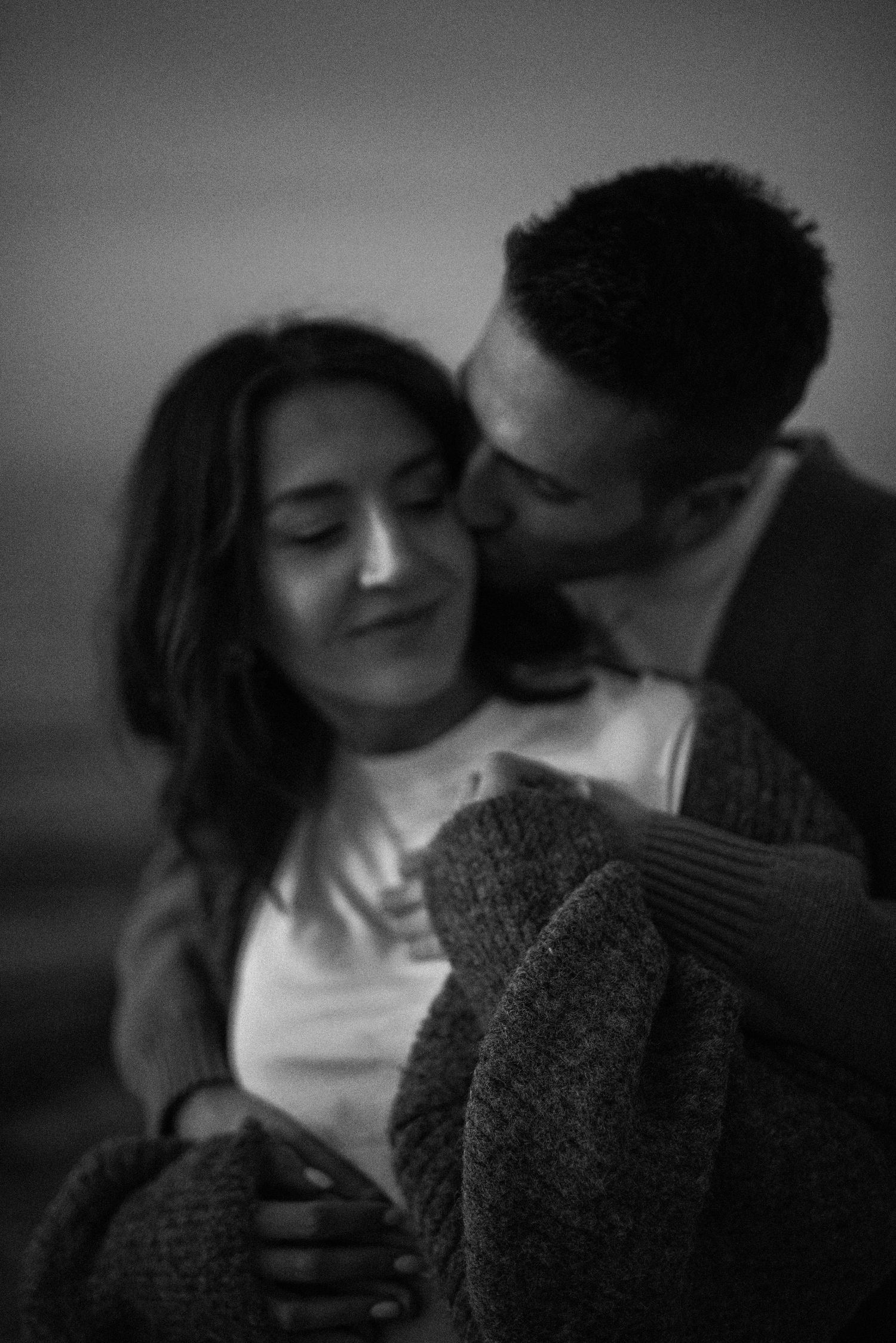 A tender black and white romantic moment between a couple embracing in soft intimate lighting.