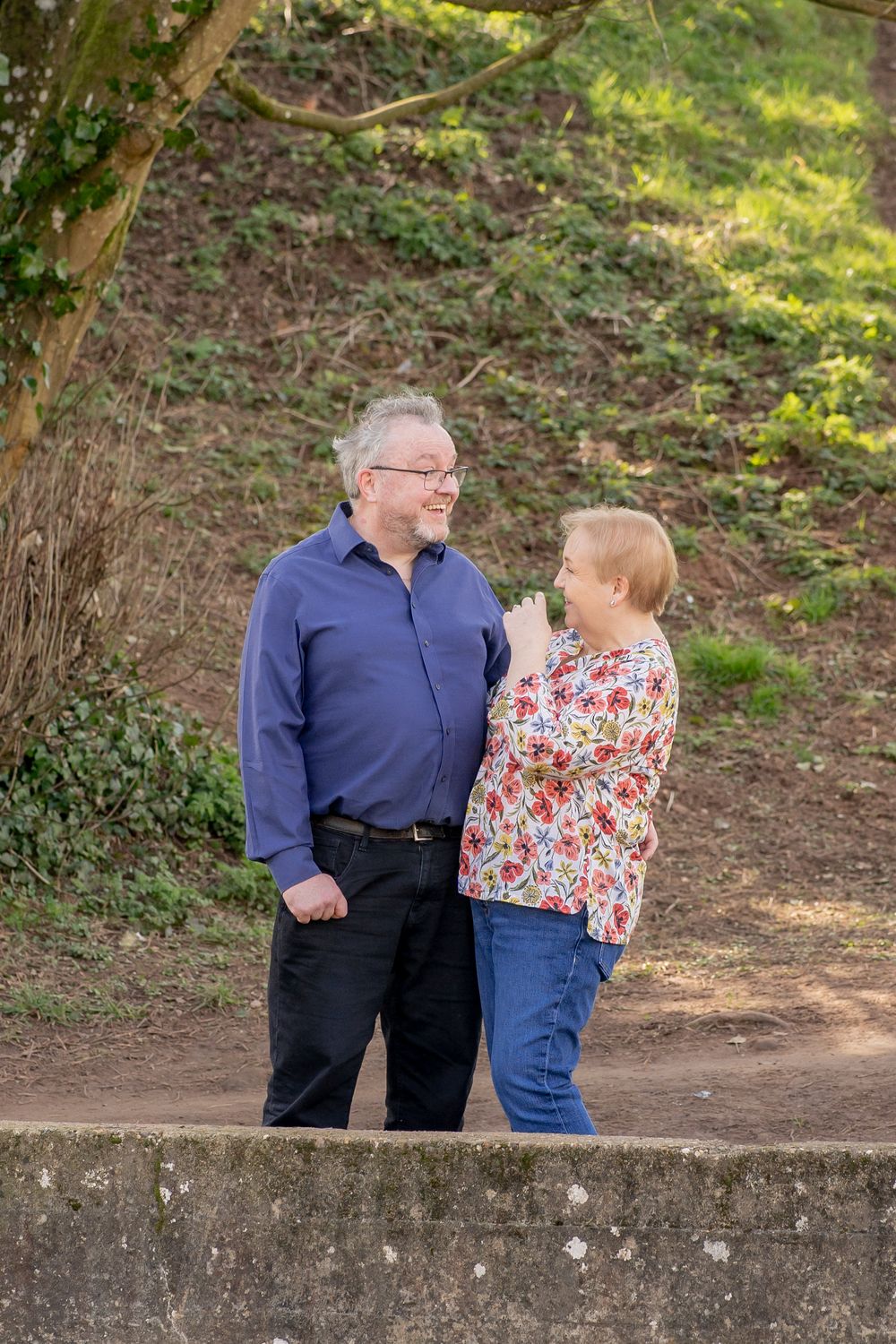 Two people enjoying a conversation while standing on a path outdoors with greenery in the background.