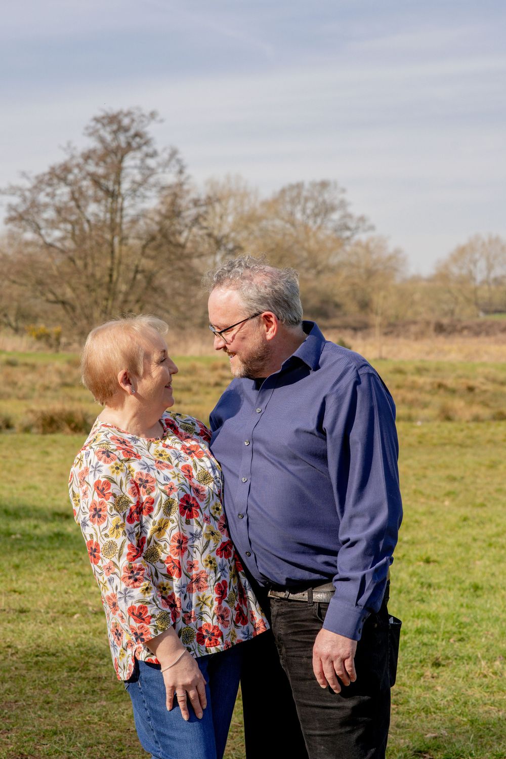 An older couple shares a loving moment outdoors in a grassy field with trees in the background.