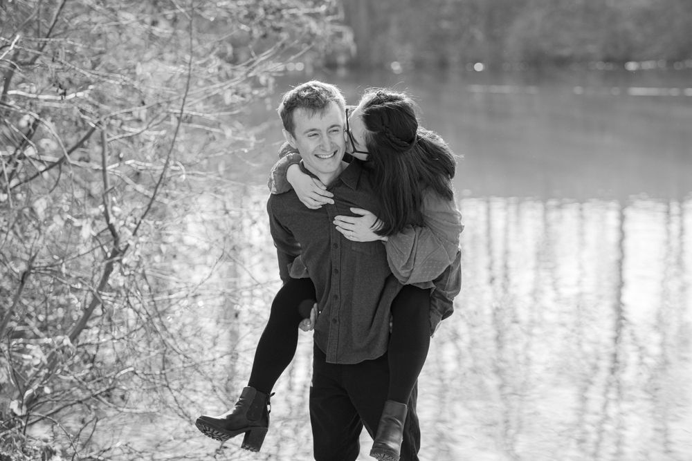 A couple shares an intimate moment by a lake on a winter day captured in black and white photography.