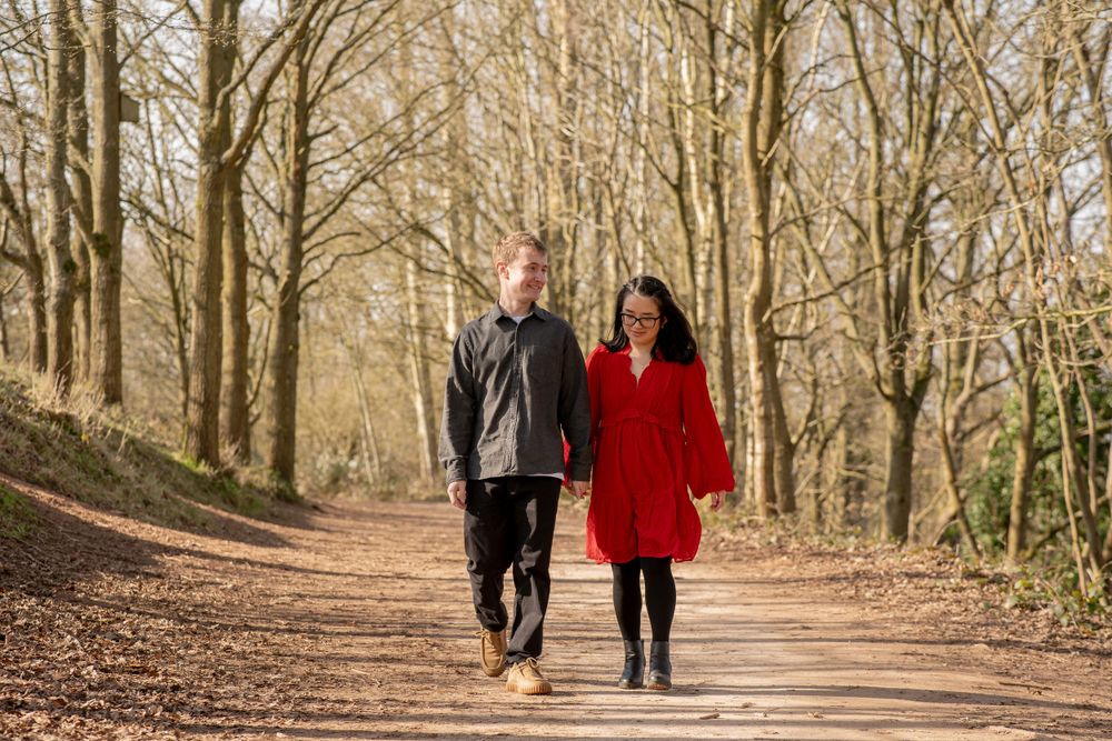 A couple walking hand in hand on a path through a scenic autumn forest with bare trees and fallen leaves.