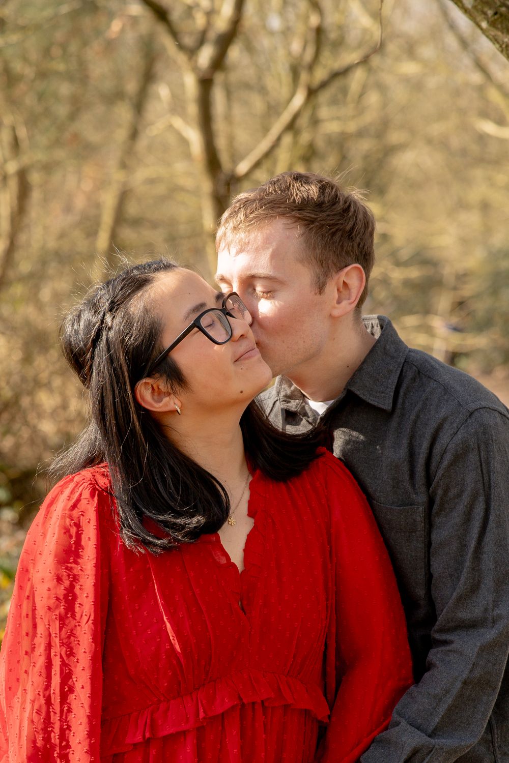 A romantic outdoor portrait of a couple sharing a tender moment in a wooded setting during autumn.