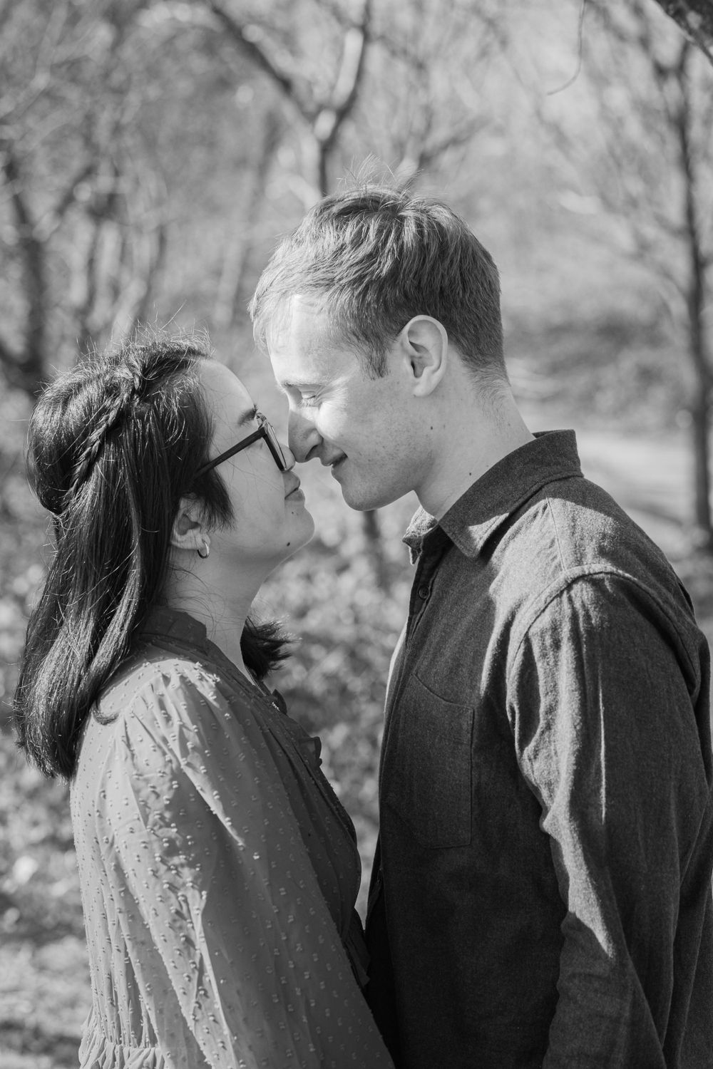 A romantic black and white portrait of a couple in a tender moment outdoors among winter trees.