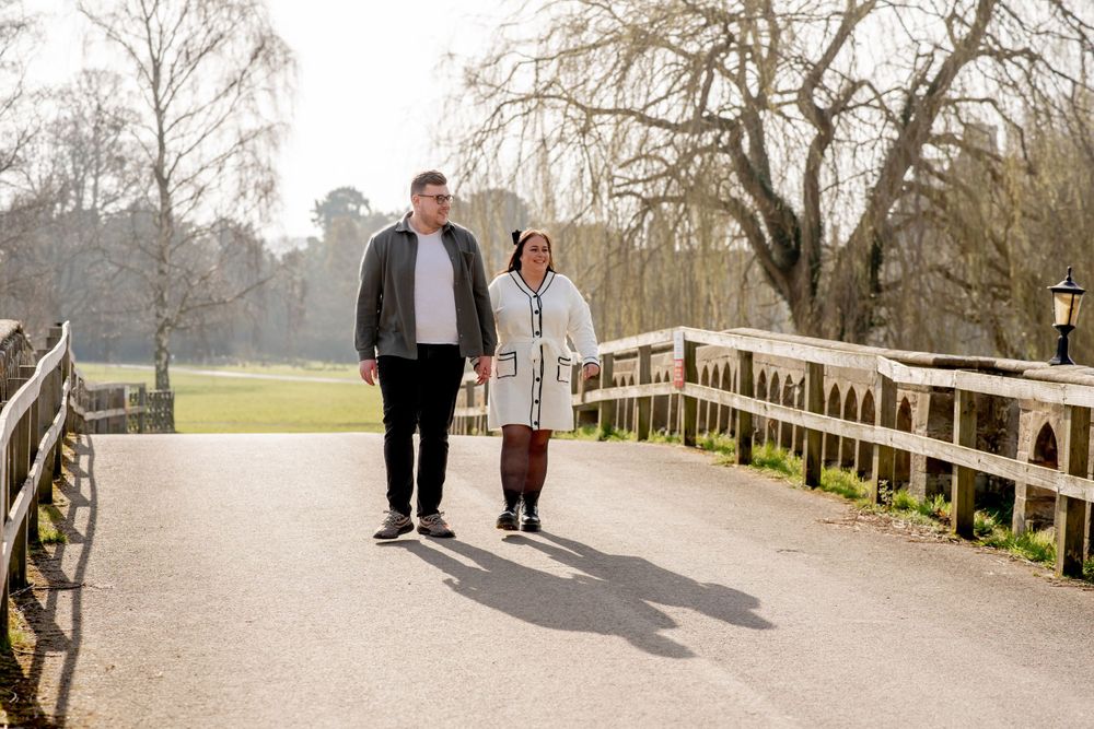 Two people take a relaxing walk together on a wooden boardwalk path surrounded by bare trees on a sunny day.