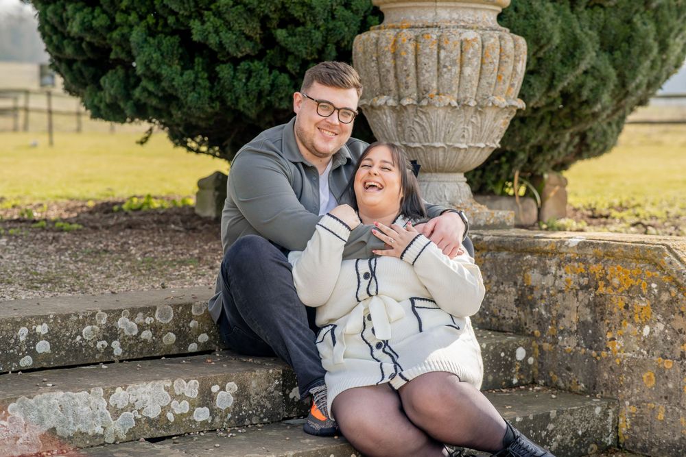 A couple sharing laughter while sitting together on stone steps near a classical garden urn.