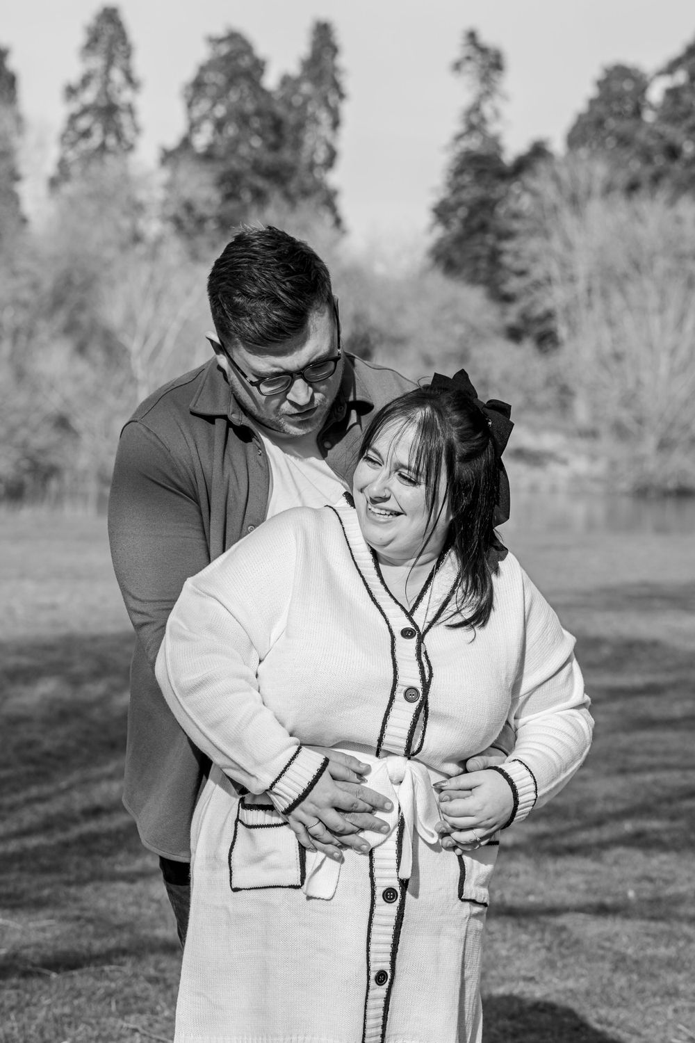 A loving couple sharing a tender moment together by a lake surrounded by evergreen trees.