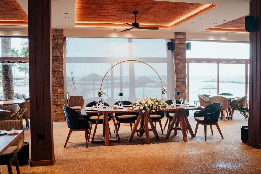 Modern coastal restaurant interior with wooden ceiling, rustic columns and ocean view dining tables decorated with flowers.
