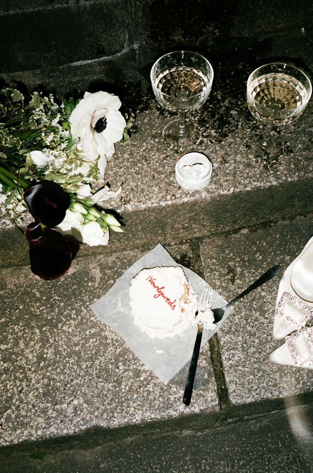 Table setting with wine glasses, white flowers, and a handwritten note on concrete surface.