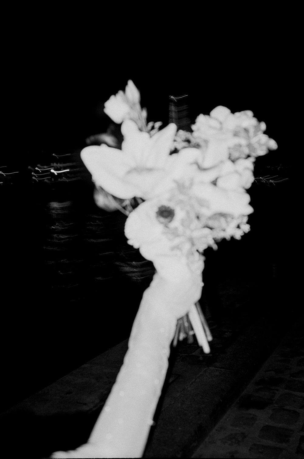 A black and white photograph shows a white bouquet of flowers being held up against a dark background.