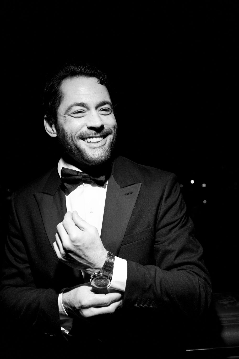 A black and white portrait of a smiling person in a tuxedo and bow tie against a dark background.