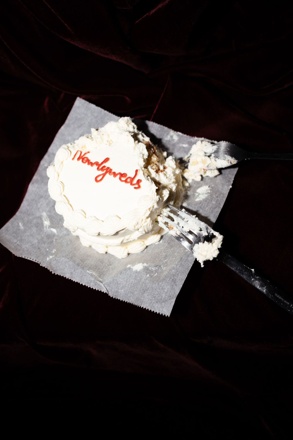 A partially eaten white frosted cupcake with red lettering sits on a paper napkin against a dark background.