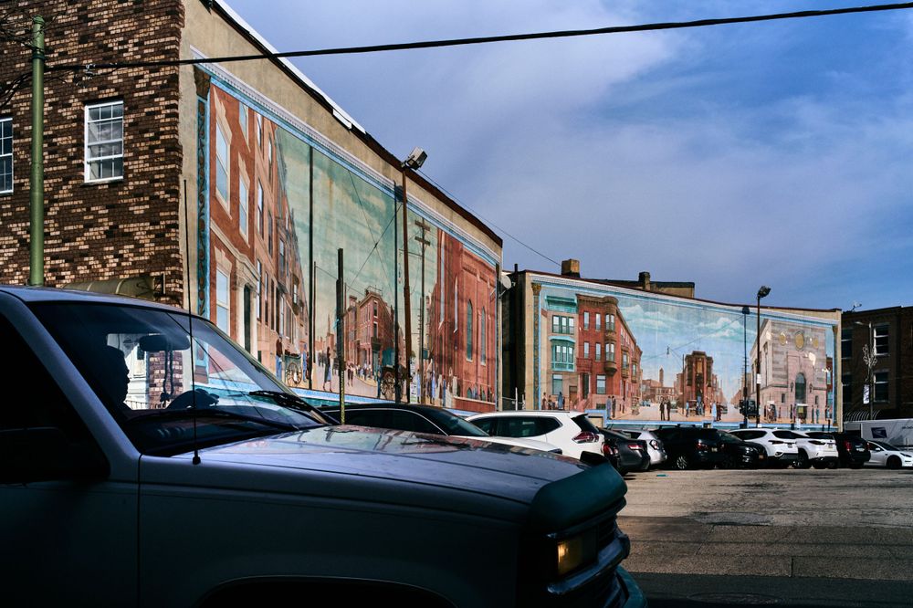 Colorful street murals painted on brick buildings with parked cars in foreground.