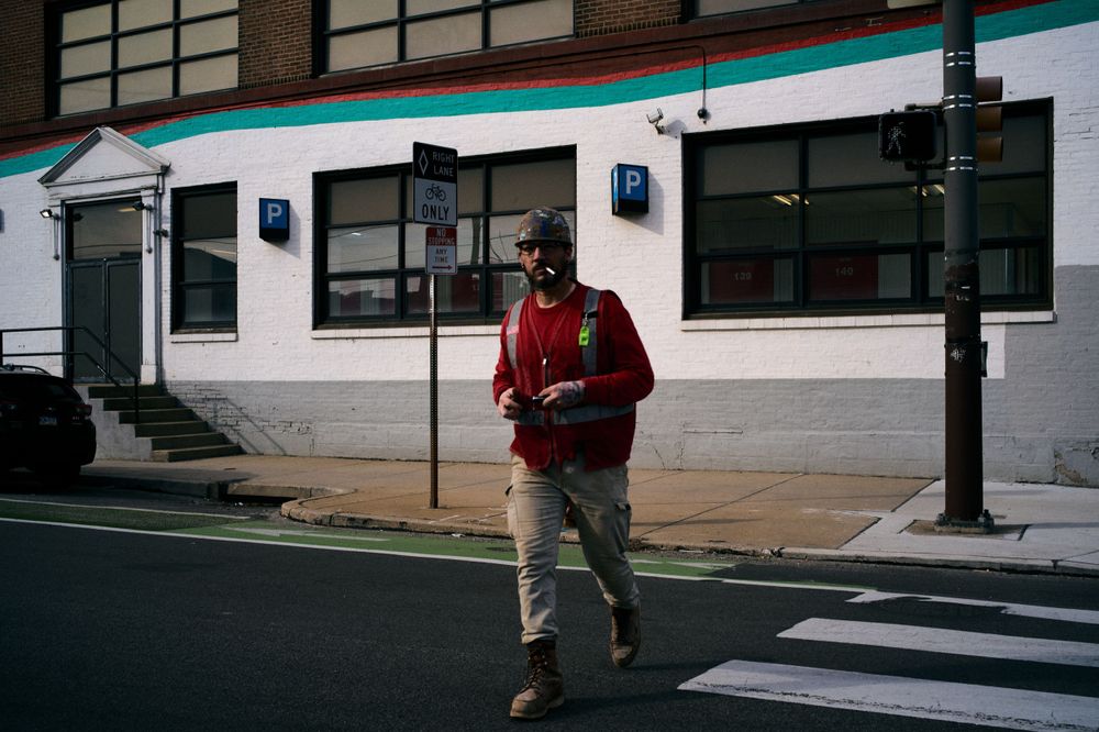 A pedestrian in red jacket crosses an urban intersection on a bright day.