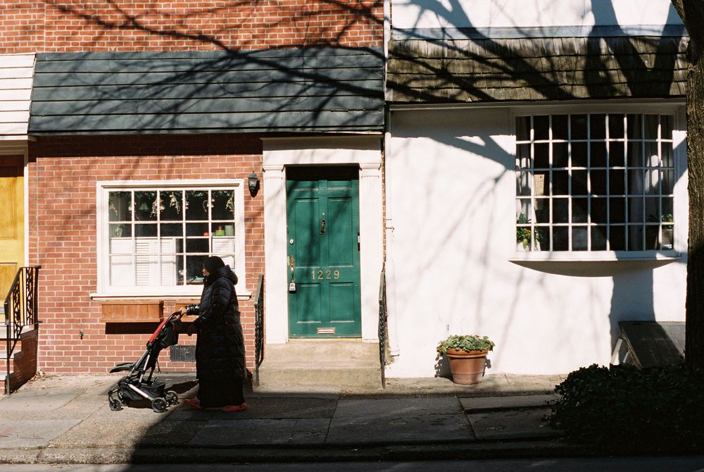 Shadow-cast street scene with colorful row houses and green door.