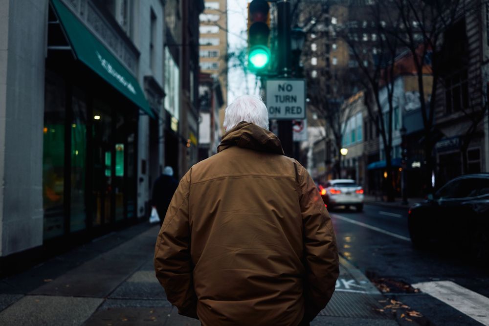 Person in brown jacket standing at crosswalk on rainy city street.
