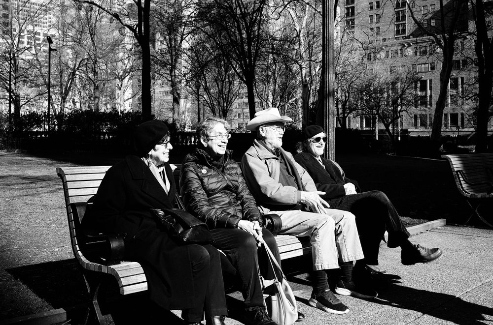Group of people sitting on park benches in a black and white photograph.
