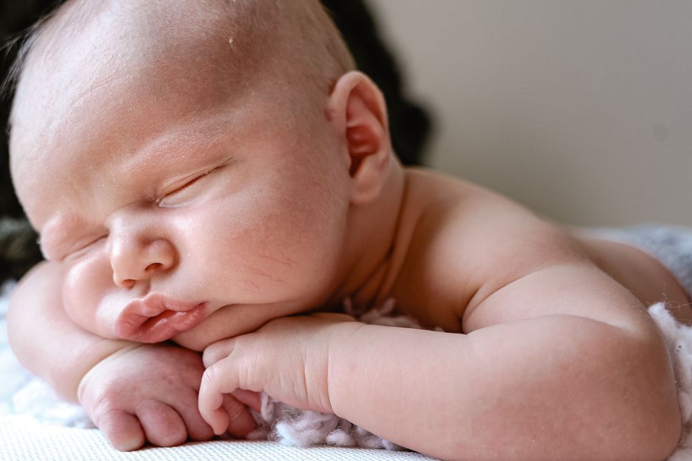 Sleeping newborn baby lying on soft blanket with hands under chin.