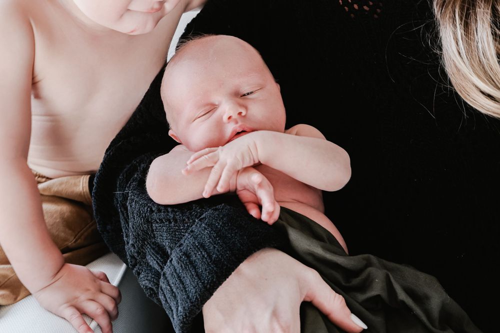 Newborn baby sleeping in dark knit outfit against black background.