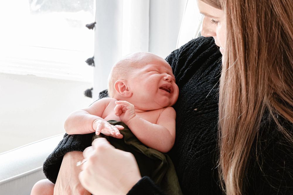 A newborn baby cradled in someone's arms near a window in black clothing.