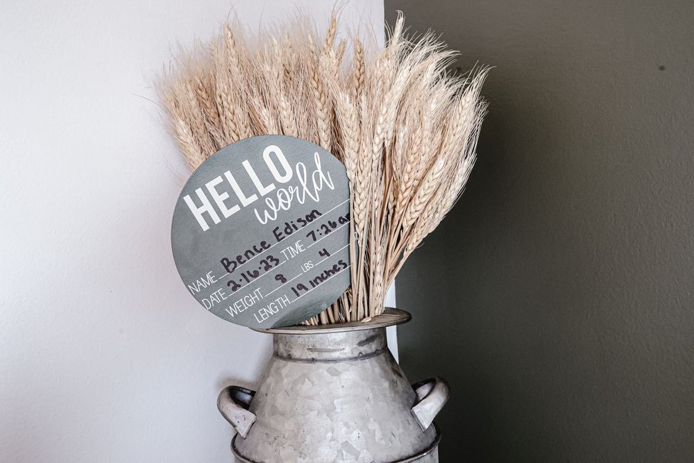 A vintage metal milk jug filled with dried pampas grass and a round Hello sign.