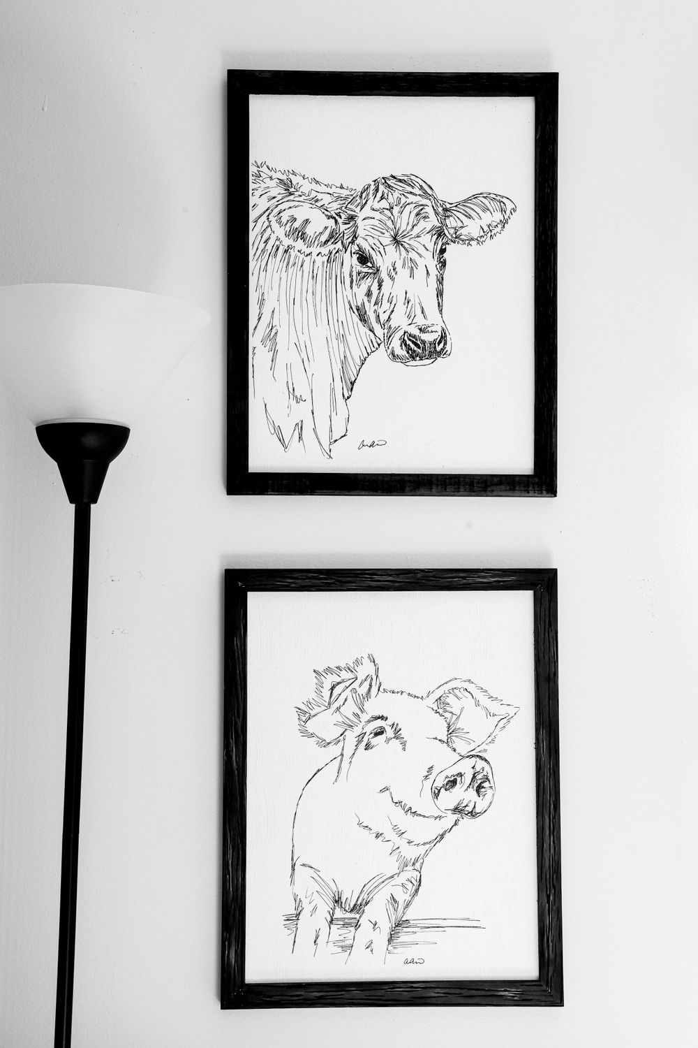 Black and white sketches of a cow and pig hanging on a wall next to a floor lamp.