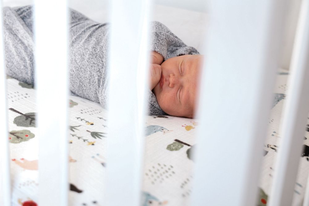 View through crib slats of sleeping infant on floral bedding.
