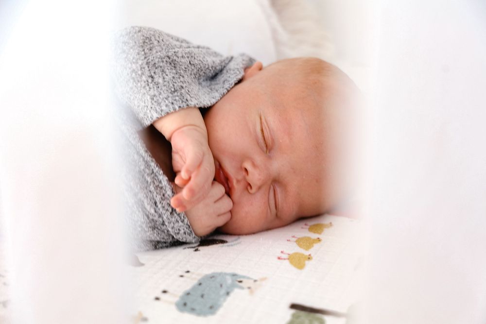 Sleeping baby in gray outfit lying on patterned sheet.