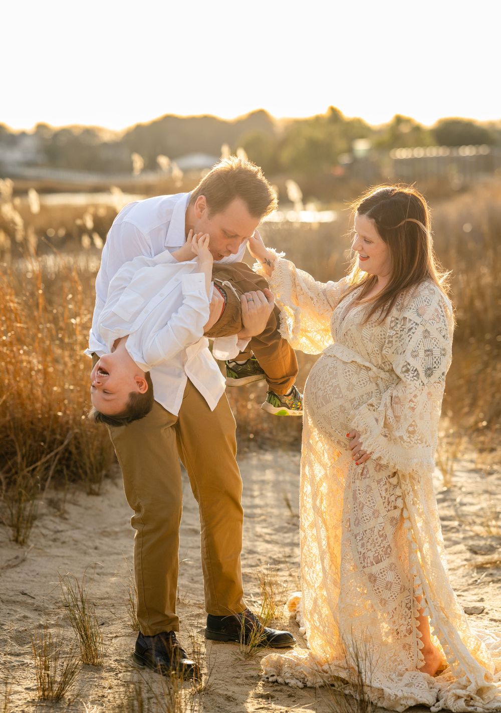 Expecting couple shares joyful moment in golden sunlit field during sunset maternity photoshoot.