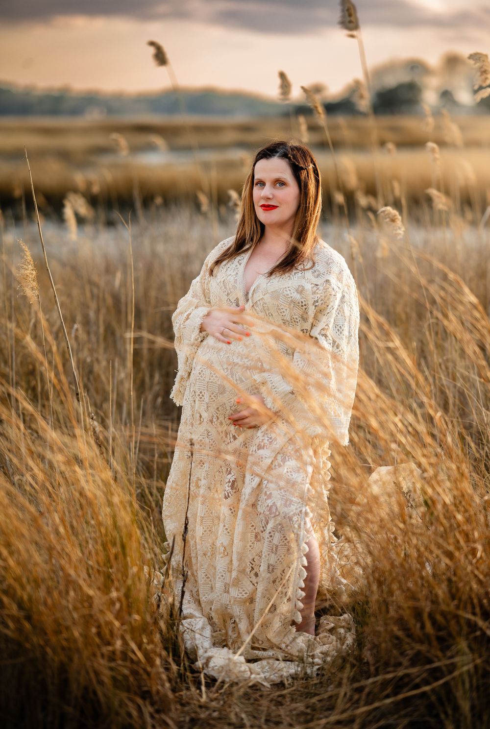 A woman wearing a lace dress stands in a golden wheat field at sunset, wrapped in soft ethereal light.
