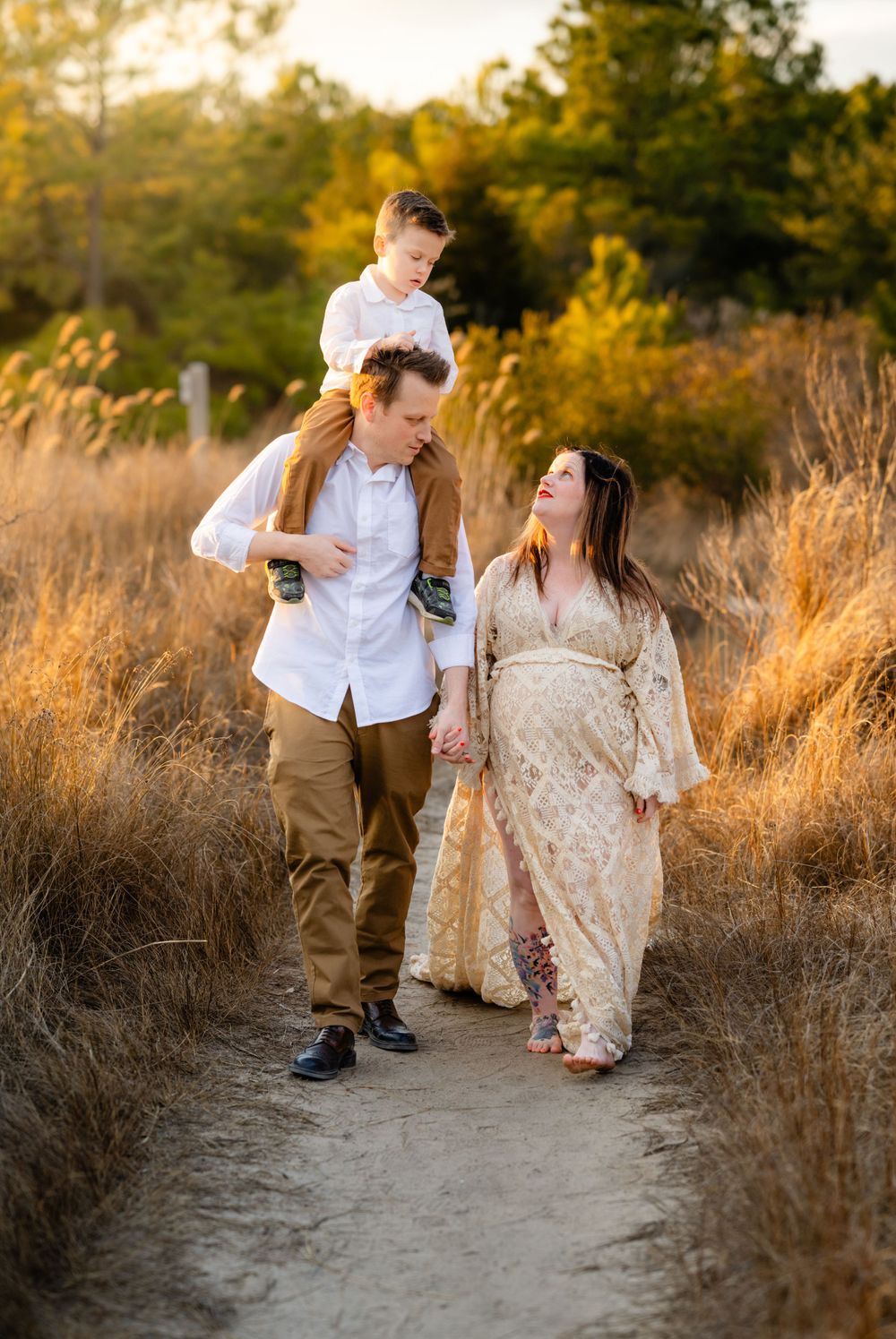 Family walks along a dirt path surrounded by golden sunlit grass during a sunset photo session.