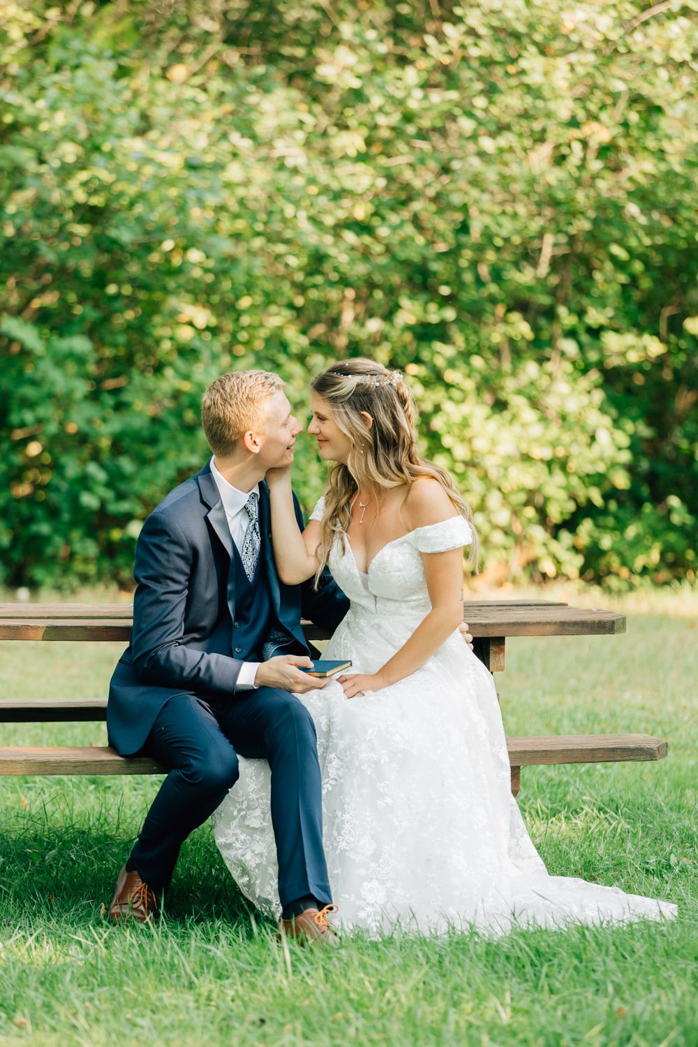 Couple shares intimate moments on wooden bench surrounded by greenery.