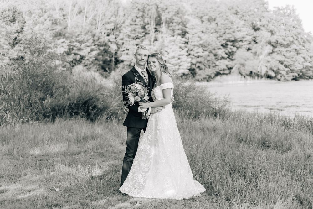 Black and white wedding photo of couple in field with trees in background.