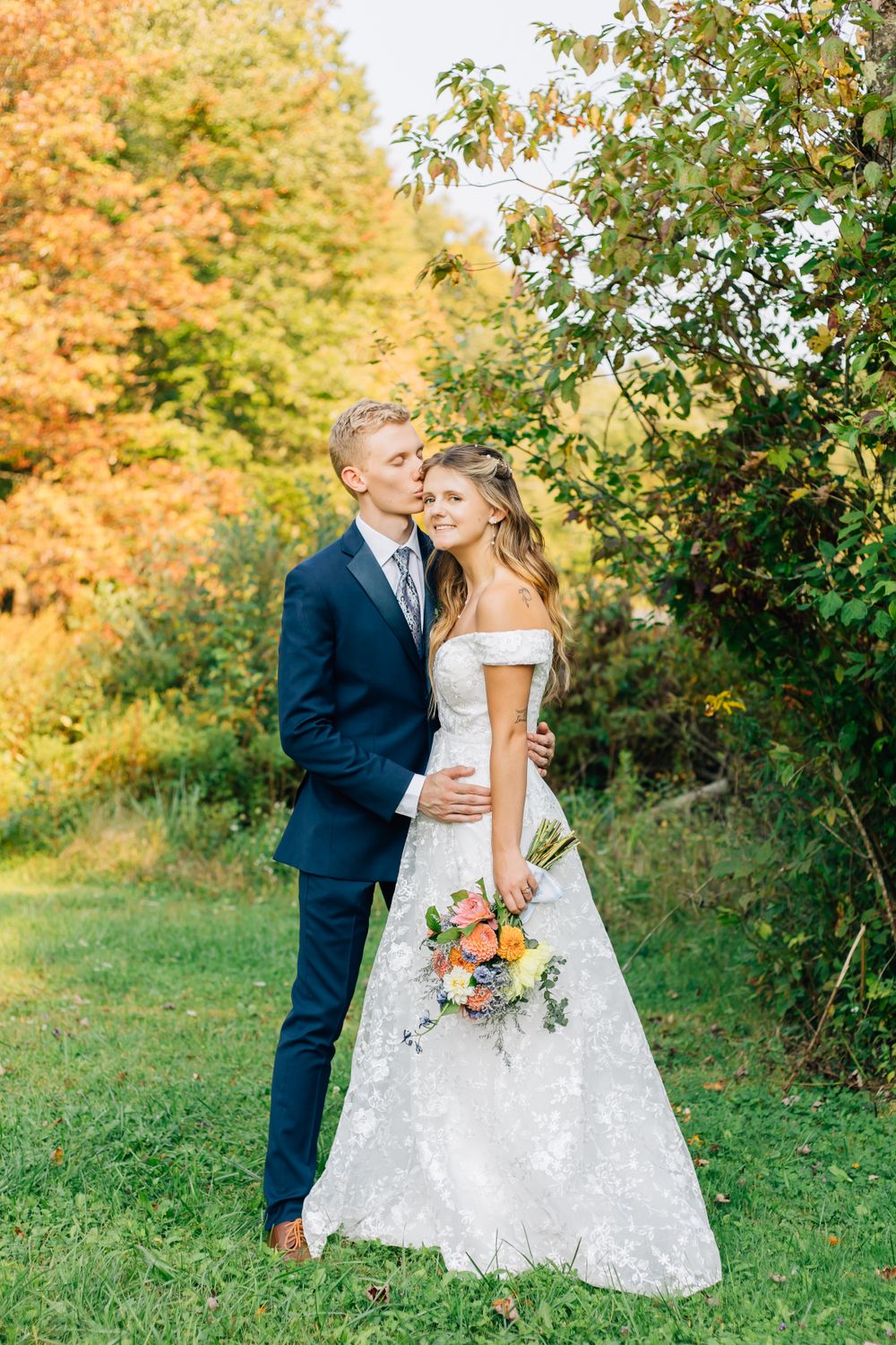 Elegant wedding couple poses in autumn garden with orange and yellow foliage.