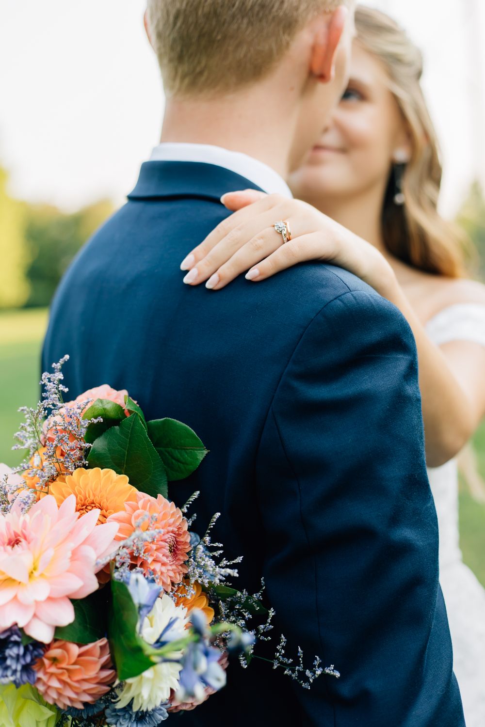 Elegant wedding flowers in pink and peach tones appear in close-up detail against a navy suit.