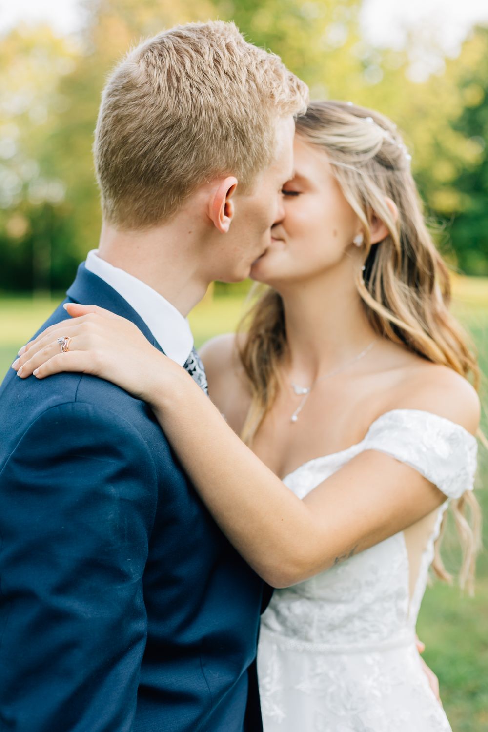 Romantic wedding couple embraces outdoors in a sunlit garden setting.