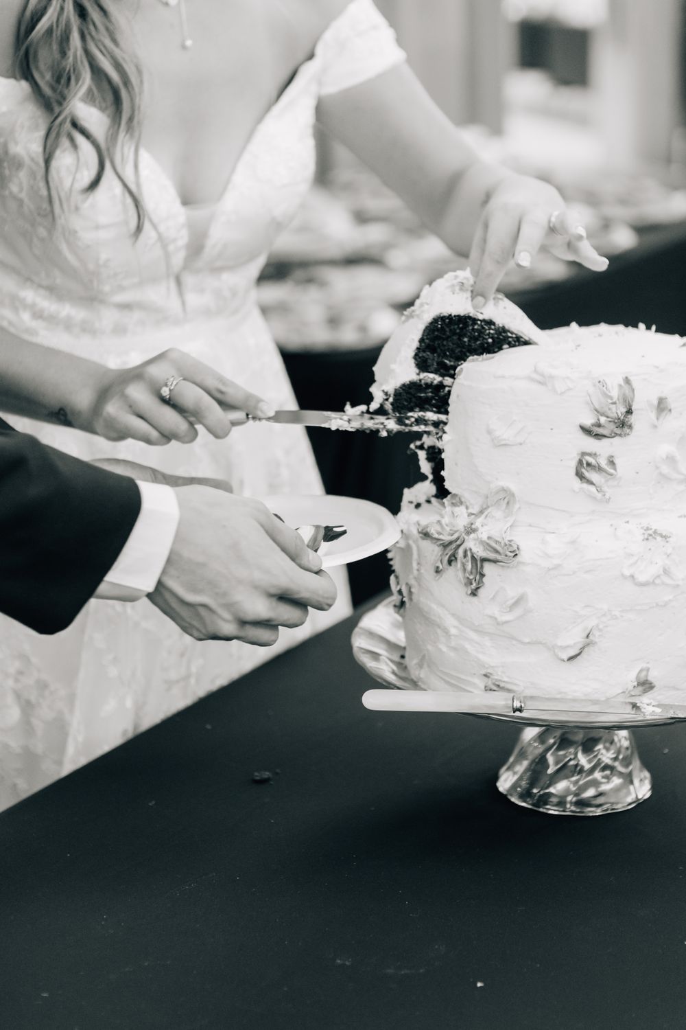 Hands decorating a white wedding cake with delicate details on a black surface.