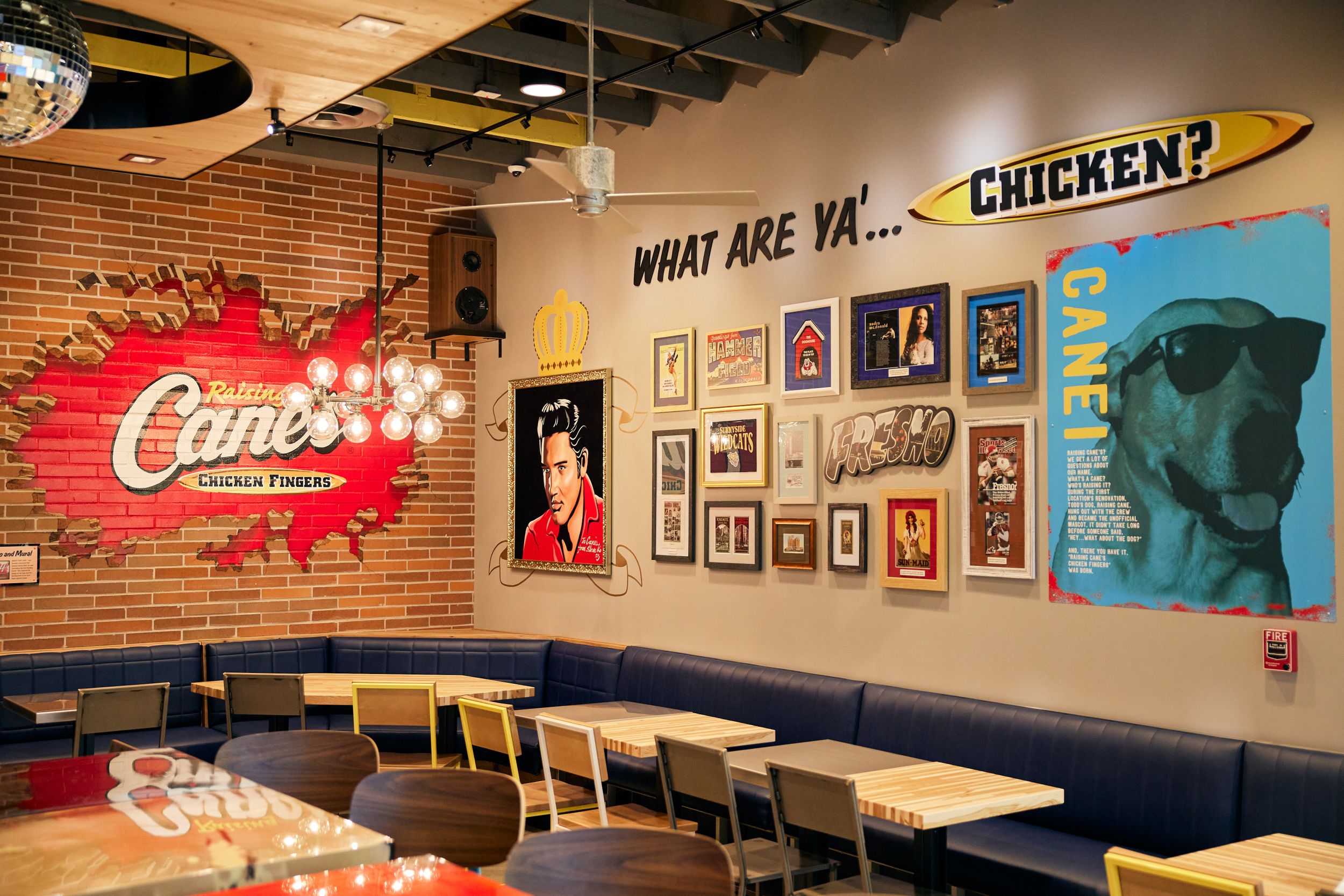 Interior of a restaurant with exposed brick walls, decorative framed artwork, and Cane's branding signage on display.