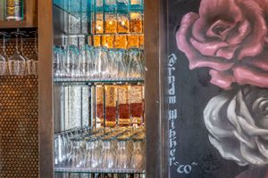 Bar display featuring glass shelving, wine glasses, and artistic rose mural on dark wall.
