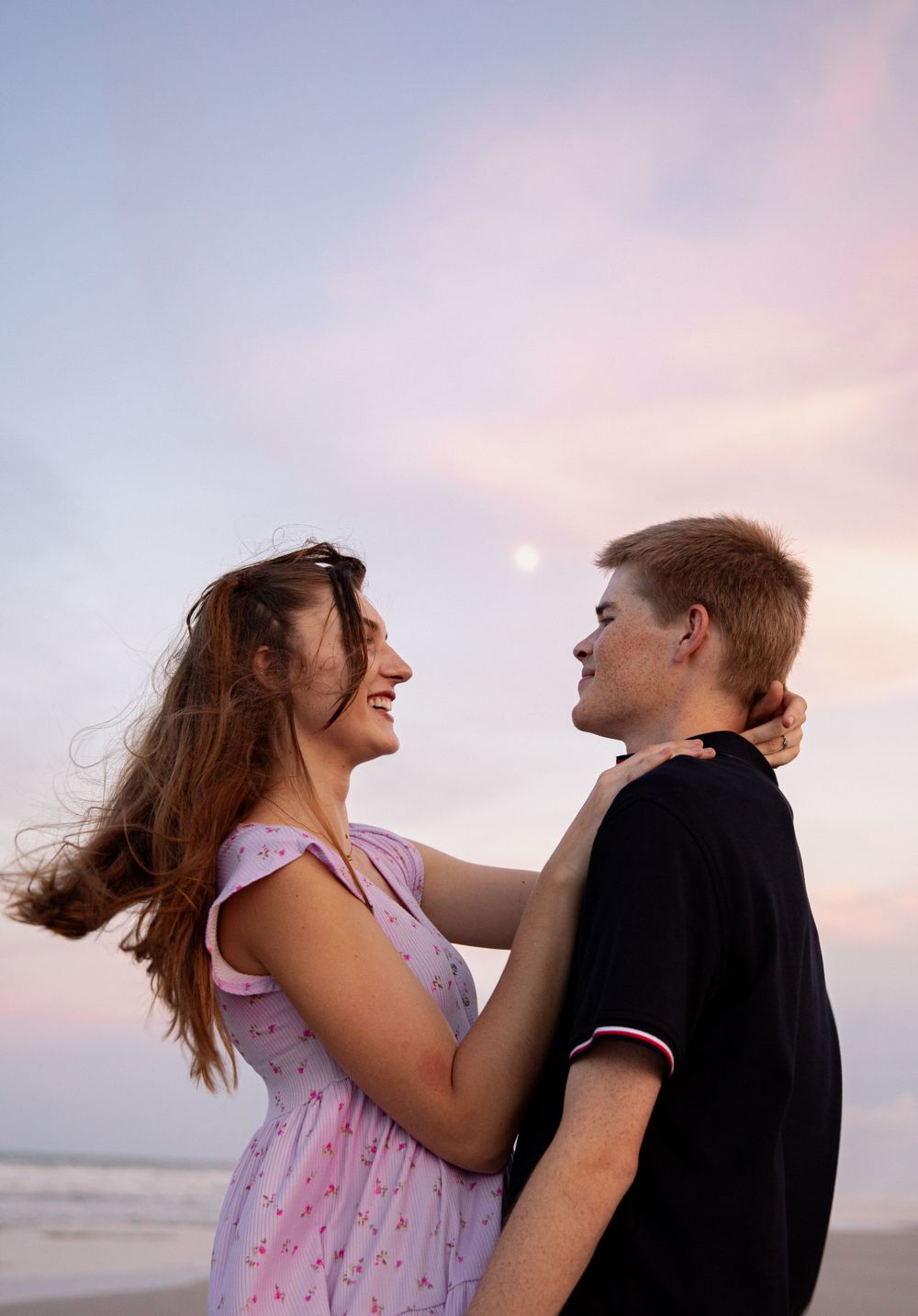 Couple embracing and laughing together on beach during sunset.