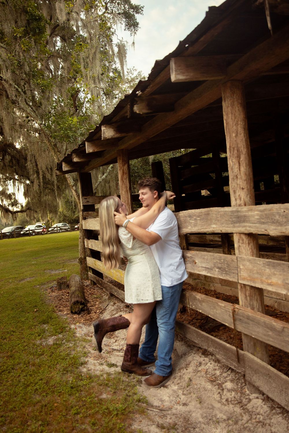 A couple shares a romantic moment together at a rustic wooden barn structure surrounded by trees and Spanish moss.