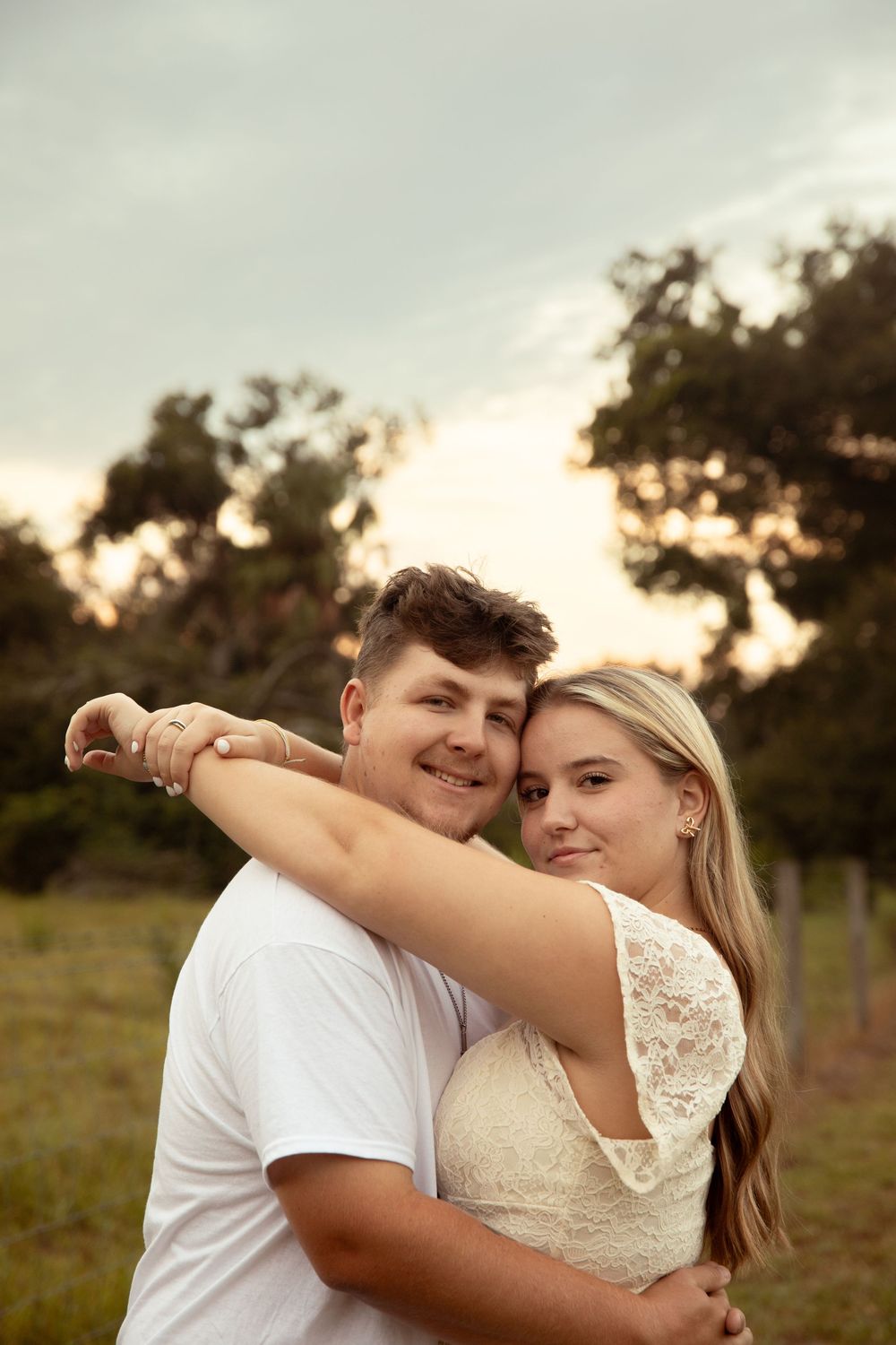 A couple embraces in a romantic outdoor photoshoot at sunset with a natural field backdrop.
