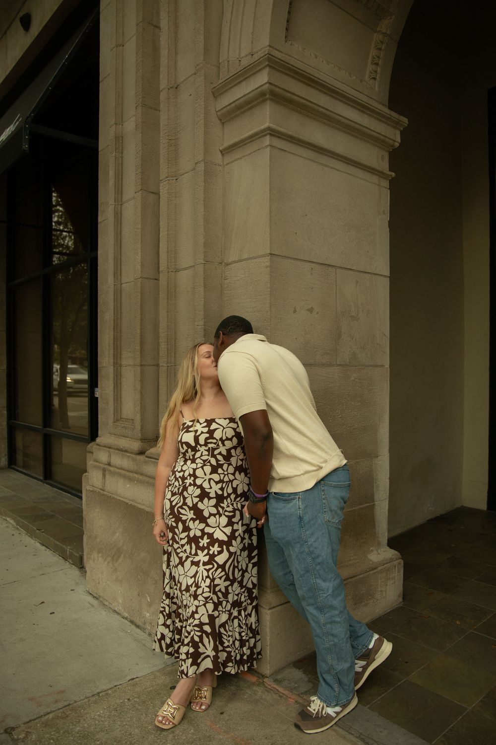 Intimate moment between couple by classical stone column in urban setting.