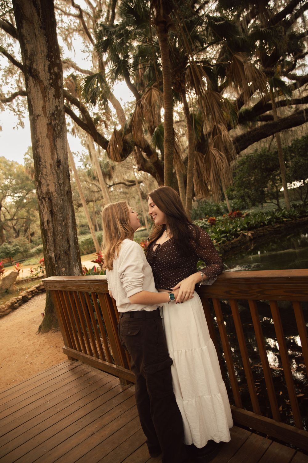 A couple shares an intimate moment on a wooden deck surrounded by tall trees at sunset.