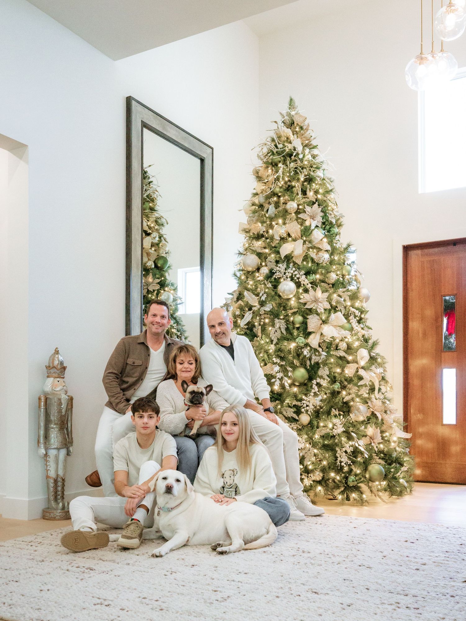 A family poses with their white dog by a decorated Christmas tree in a bright modern living room.