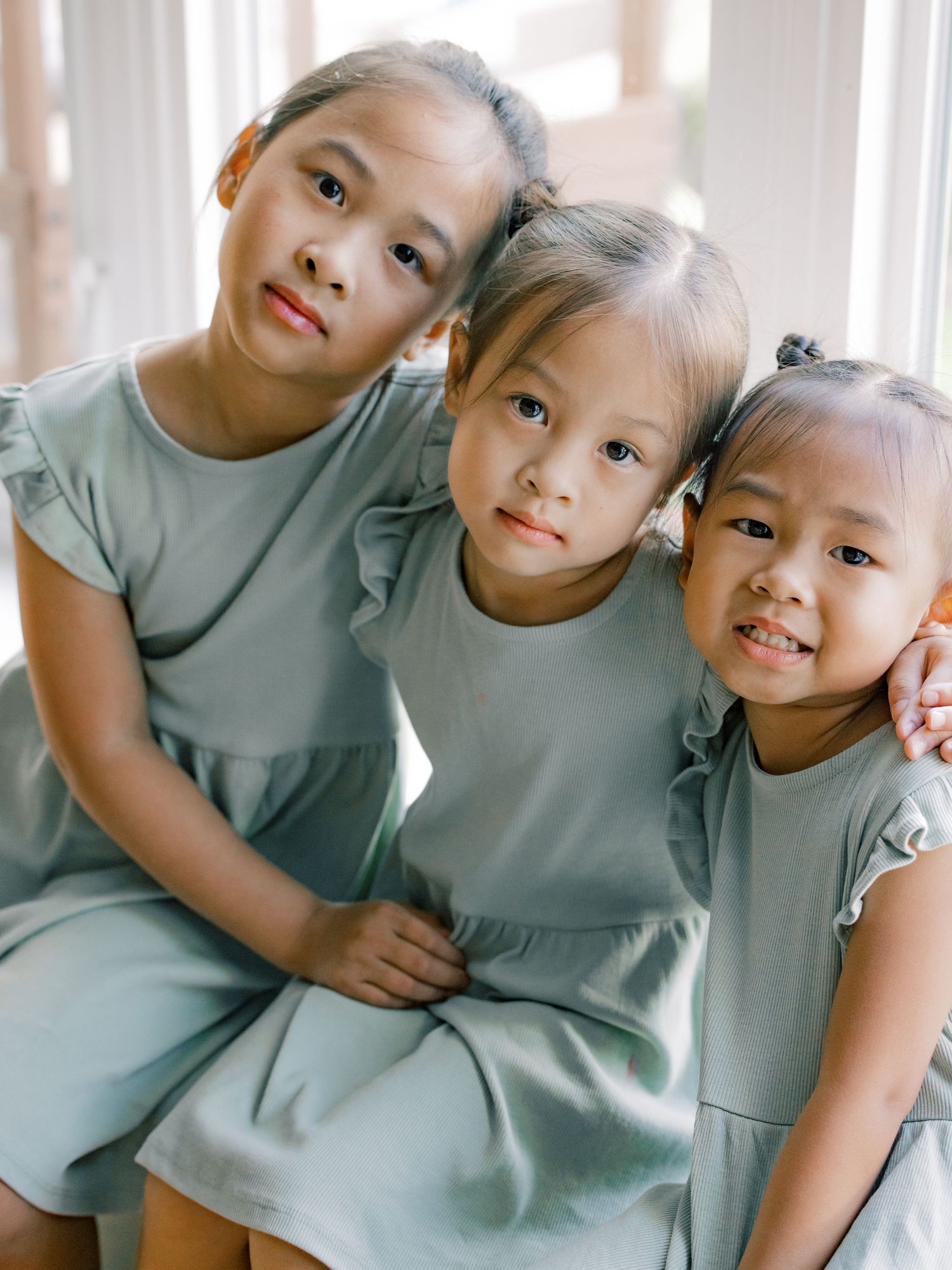 Three children wearing matching mint green dresses pose together in a warm indoor setting.