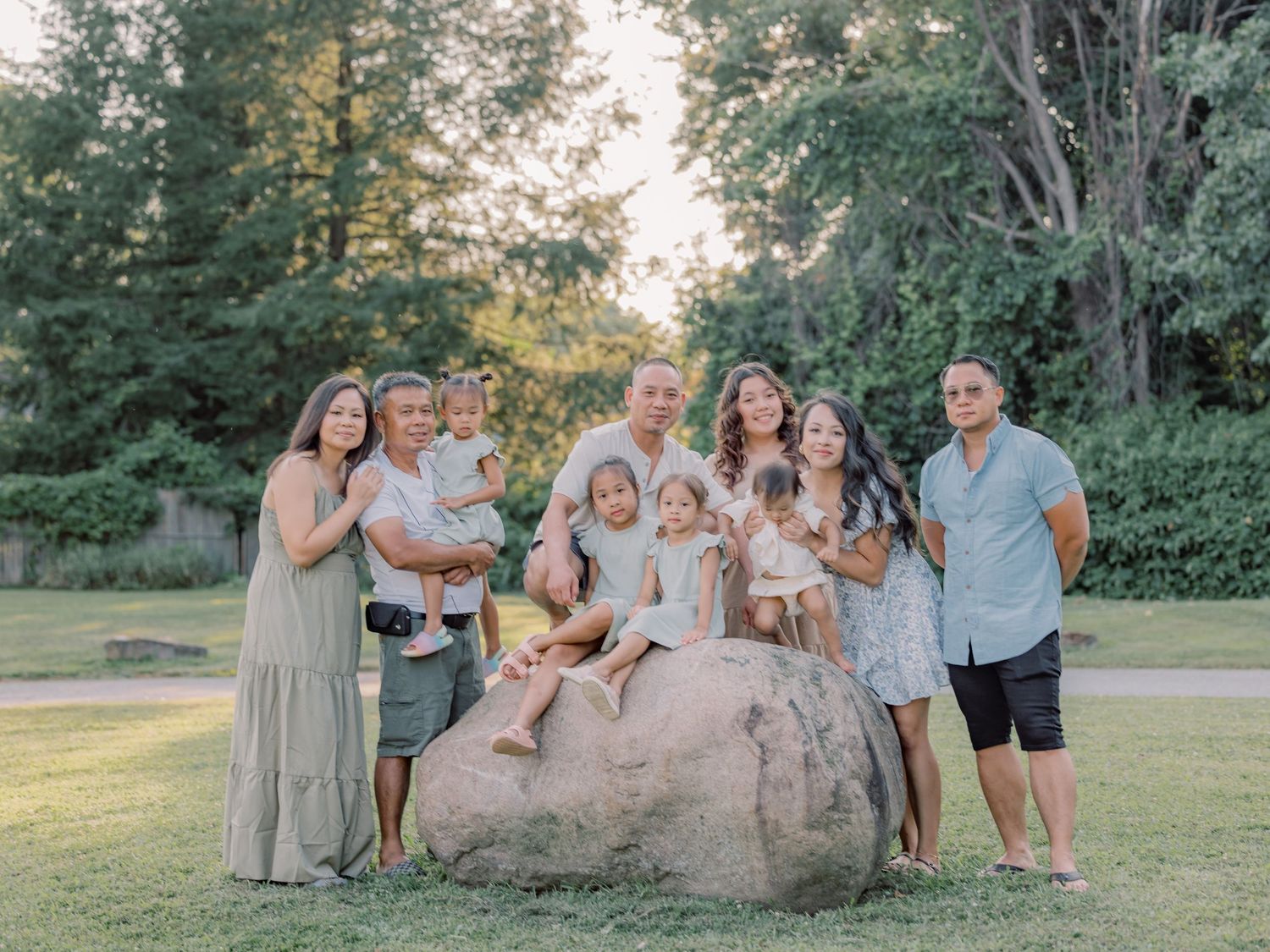 A group stands together posing for a family portrait outdoors on a large boulder at sunset in a park setting.