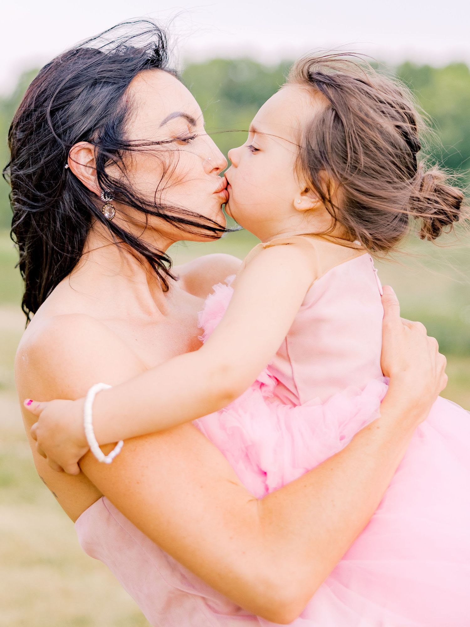 A tender moment captured outdoors as two people share a loving kiss against a soft natural background.