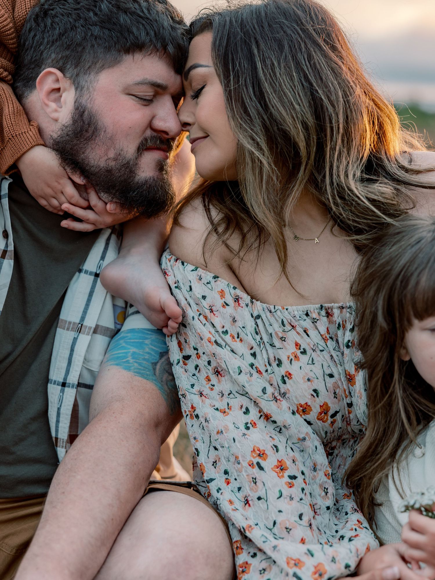 A romantic couple sharing an intimate moment while wearing floral dress and plaid shirt at sunset.
