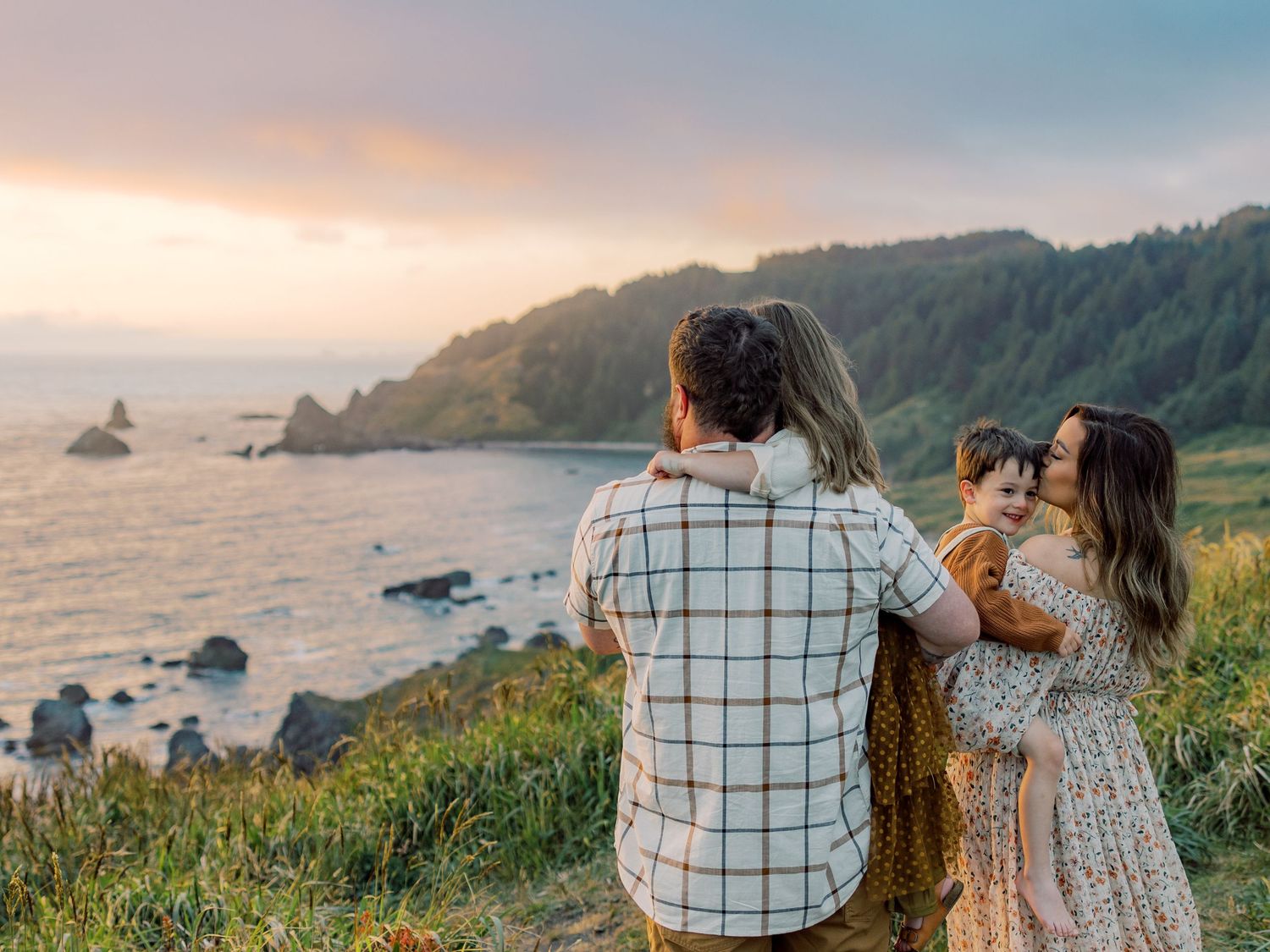 Couple enjoying sunset views from coastal cliffs overlooking a rocky Pacific Northwest beach at golden hour.